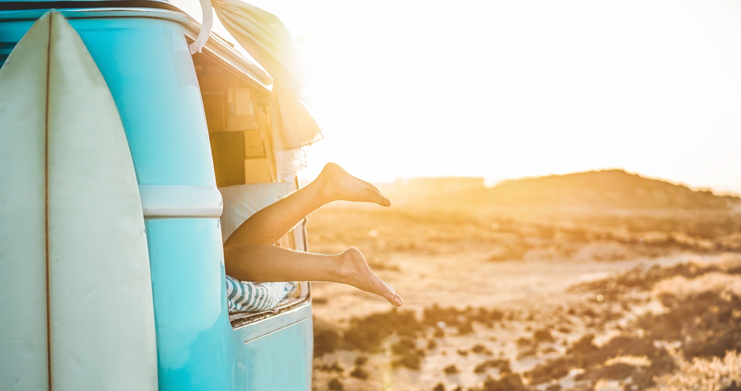 Legs view of happy surfer girl inside minivan at sunset - Young woman having fun on summer vacation - Travel,sport and nature concept - Focus on feet