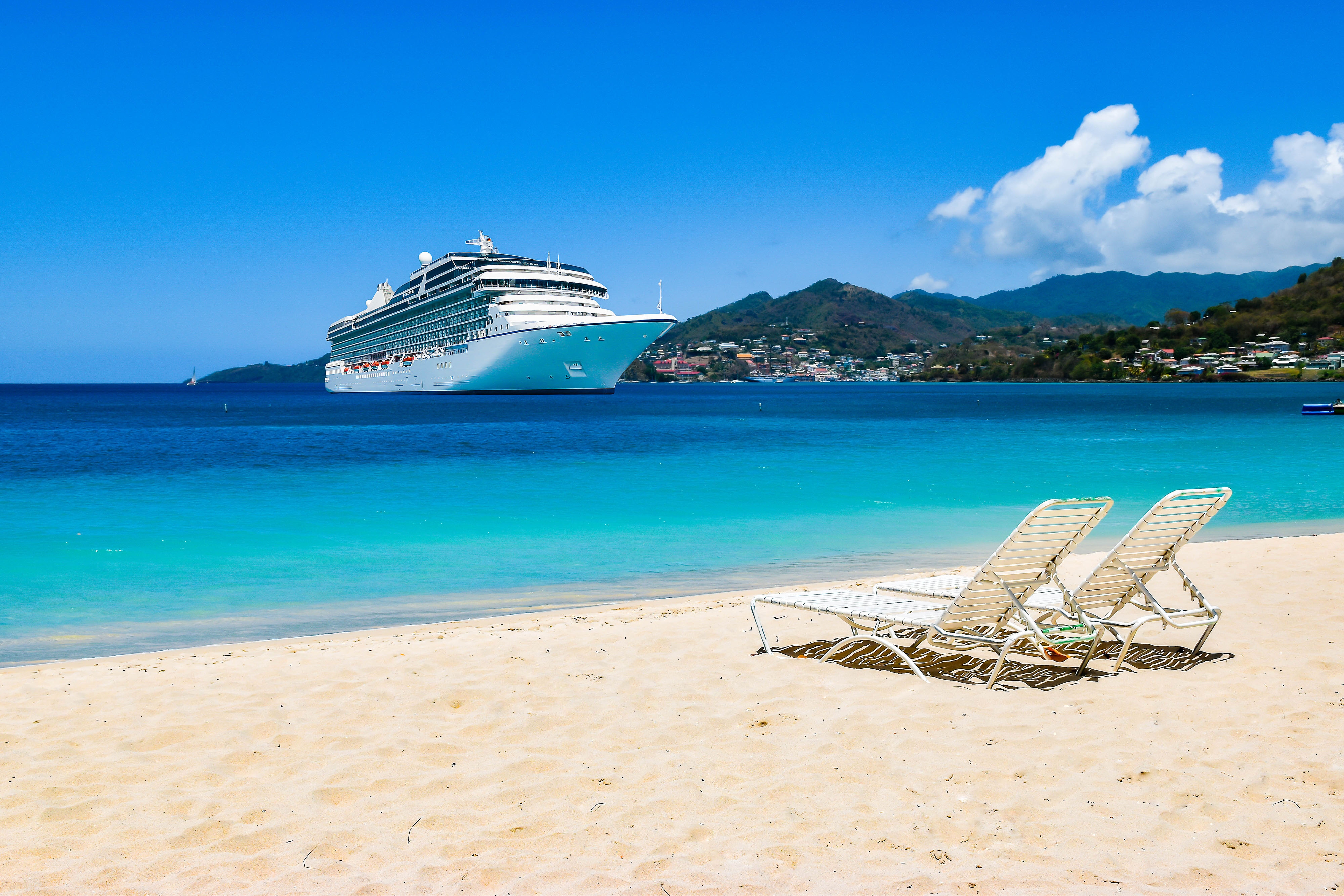 Cruise ship in Caribbean Sea with beach chairs on white sandy beach 